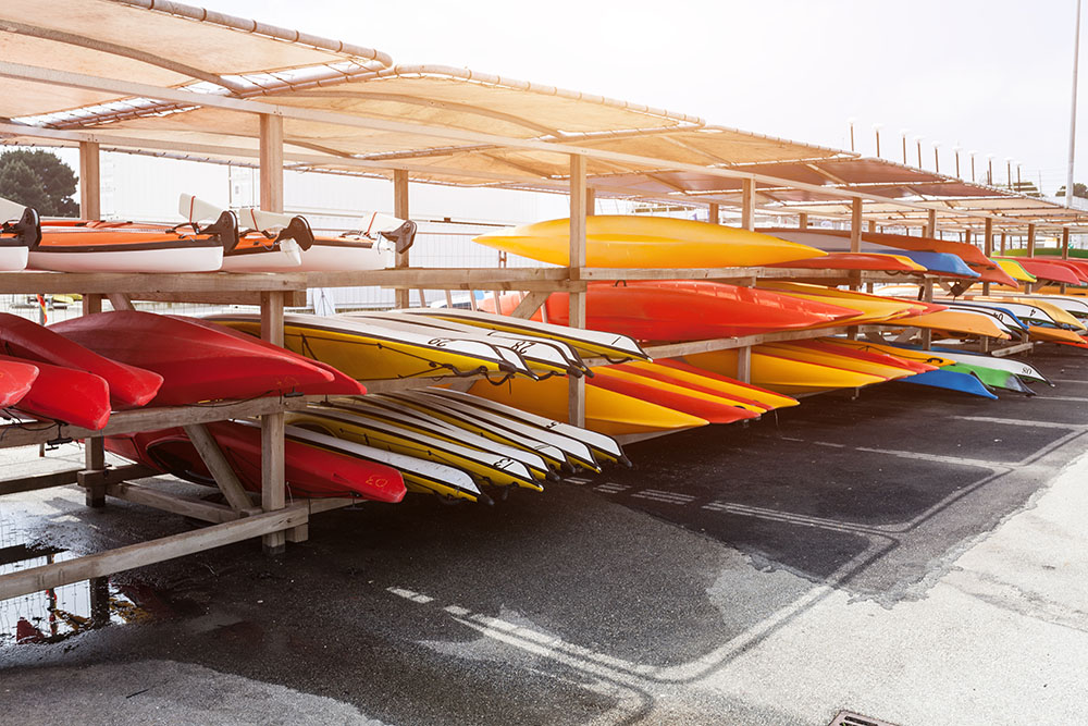 In sunlight, red, yellow and white kayaks placed upside down on metal storage racks. Stocked canoe in the Brest, France 28 May 2018.