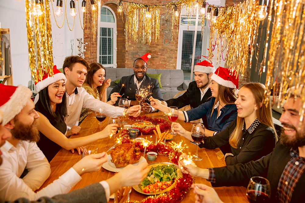 Happy co-workers celebrating while company New Year and Christmas party. Young caucasian people in celebrate attire with sparklers talk, drink wine, cheers. Concept of office culture, teamwork, winter