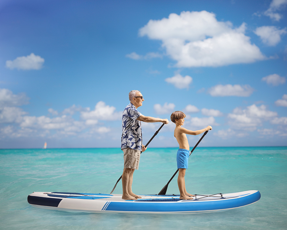 Full length profile shot of a boy and elderly man paddling a SUP board together in the sea