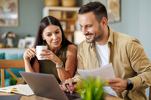 Married couple sit at a table in the living room with laptop,working from home office. Online meeting.