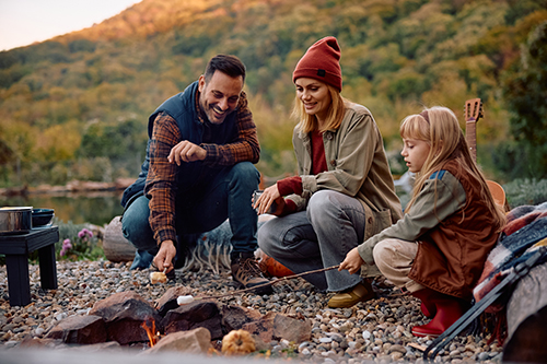 Happy family roasting marshmallows while gather around campfire in nature.