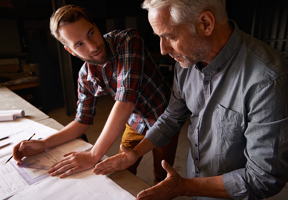 Carpenter, team and men with blueprint for discussion of construction project or father teaching son. Engineer, apprentice and senior mentor with design, drawing and planning for training at workshop