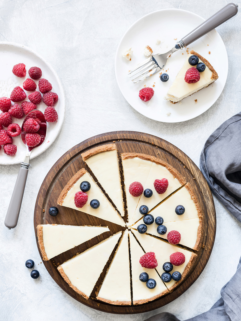 Classic New York cheesecake with fresh raspberries and blueberries on white concrete background, top view