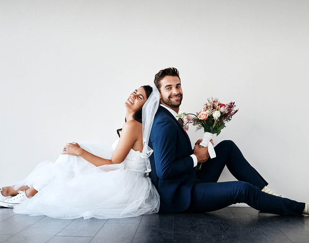 You can lean on me any day. Studio shot of a newly married young couple sitting back to back on the floor against a gray background.