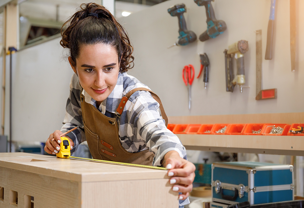 Young Latin female carpenter using a tape measure to measure dimensions to cut wood. to make furniture in the carpentry workshop Concept of young people start up and SME small business concept
