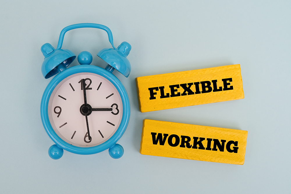 A coloured wooden block with text FLEXIBLE WORKING next to blue alarm clock