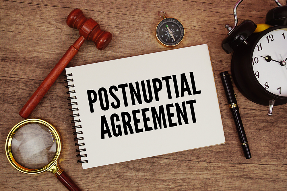 Postnuptial Agreement message written on notepad with alarm clock, wood gavel and magnifying glass flat lay on wooden background