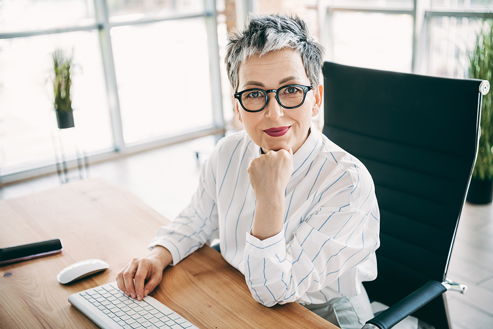 Confident mature woman in a professional office environment working with a computer, emphasizing success, career-focused attitude, and professional workspace.