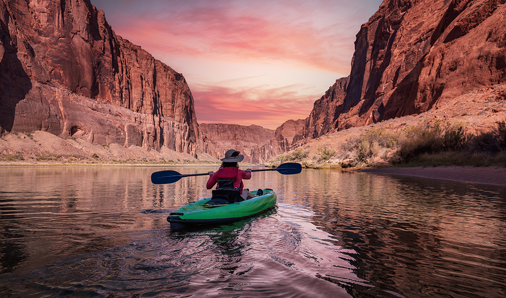 Adventurous Woman on a Kayak paddling in Colorado River. Glen Canyon, Arizona, United States of America. Sunrise Sky Art Render. American Mountain Nature Landscape Background.