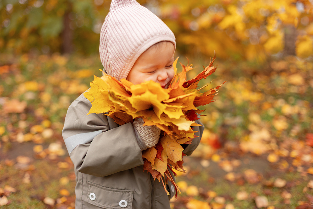 Baby girl enjoying autumn leaves, child having fun with colorful autumn foliage