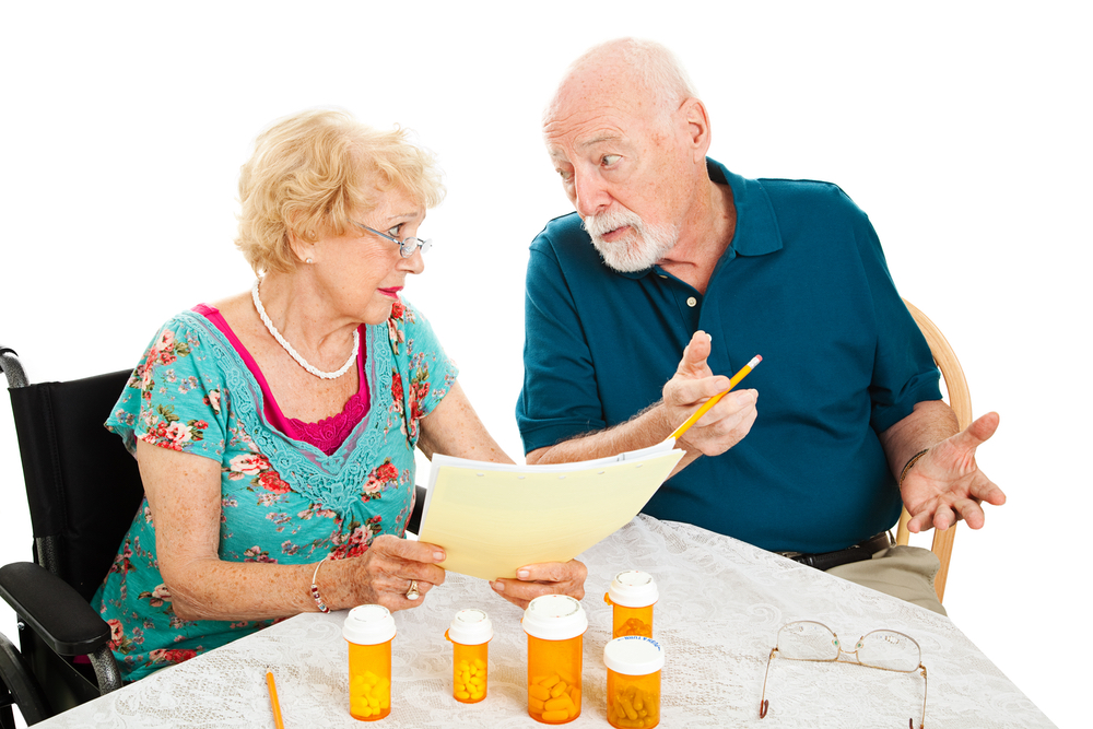 Senior couple at the dining room table discussing medical and prescription costs.  White background.  
