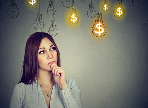 Portrait thinking young woman looking up at dollar idea light bulbs above head isolated on gray wall background 