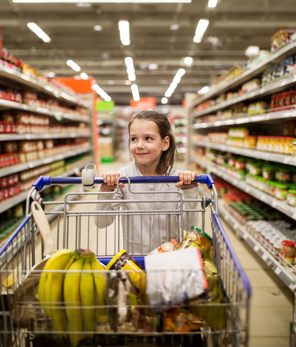 sale, consumerism and people concept - happy little girl with food in shopping cart at grocery store