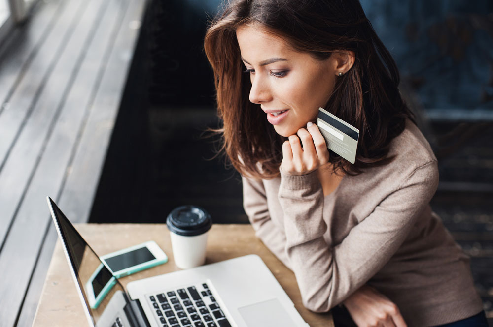 Young woman holding credit card and using laptop computer. Businesswoman or entrepreneur working at home. Online shopping, e-commerce, internet banking, spending money, working from home concept