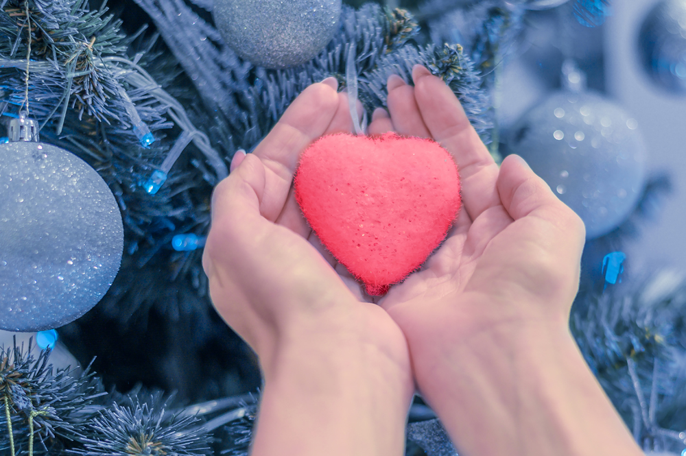female hands hold heart on christmas tree