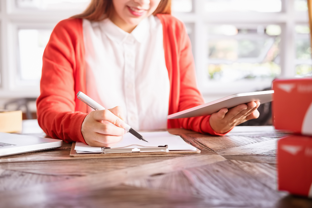 Beautiful young asian business owner working using computer and tabet smiling while standing in workshop.Responding on business e-mail,taking customer orders.