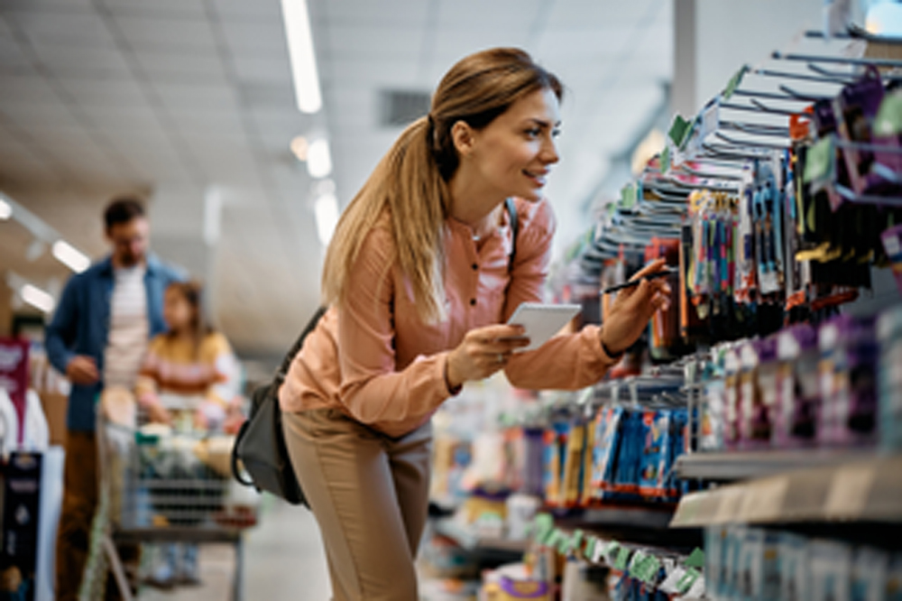 Smiling mother going through checklist while choosing school supplies for her daughter in supermarket. 