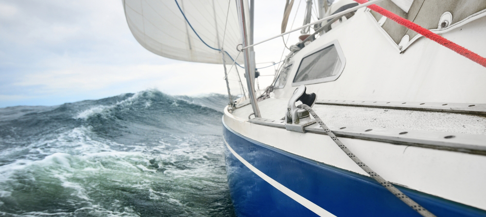 Yacht sailing in a thunderstorm on a rainy day. Close-up view from the deck to the bow, mast and sails. Dramatic stormy sky, dark clouds. Waves and water splashes. Rough weather. Baltic sea, Sweden