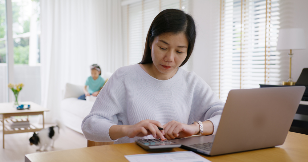 Adult asia people single mom small SME owner support happy sit busy apply child tax credit refund plan form app or pay loan bill on laptop. Little kid girl play at home hybrid job career workforce.