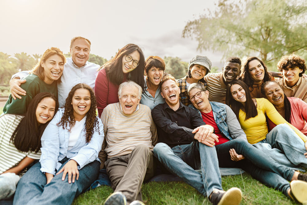 Happy multigenerational people having fun sitting on grass in a public park - People diversity concept