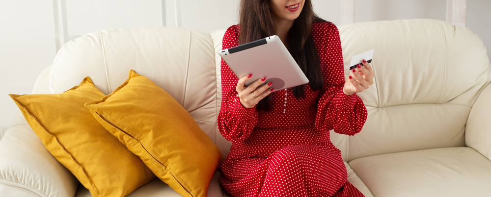 Banner Woman happily shops online sitting on a sofa with tablet, copy space and card. Convenience and ease of digital consumerism