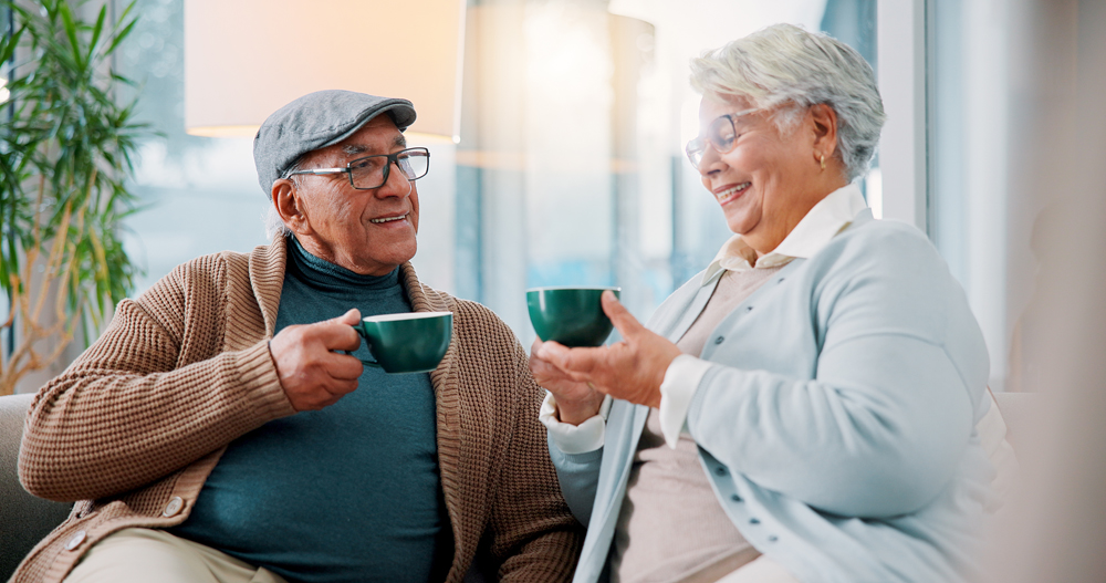 Home, senior couple and drinking coffee with conversation, relax and enjoy latte together. Old man, happy woman and tea cup in living room for retirement, love or morning chat for marriage on weekend