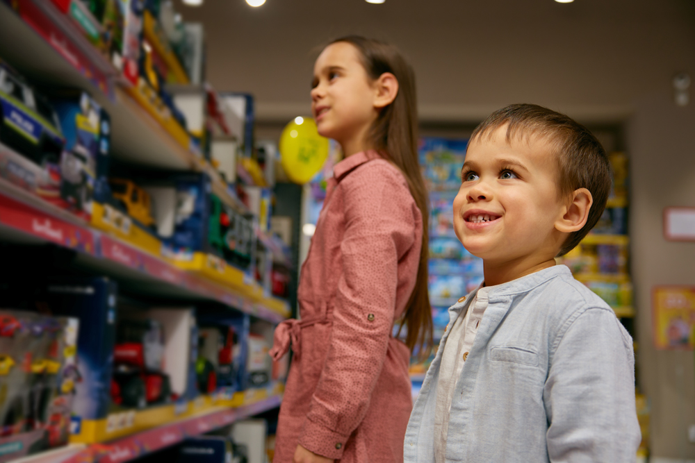 Happy little children walk among display cases with toys in store