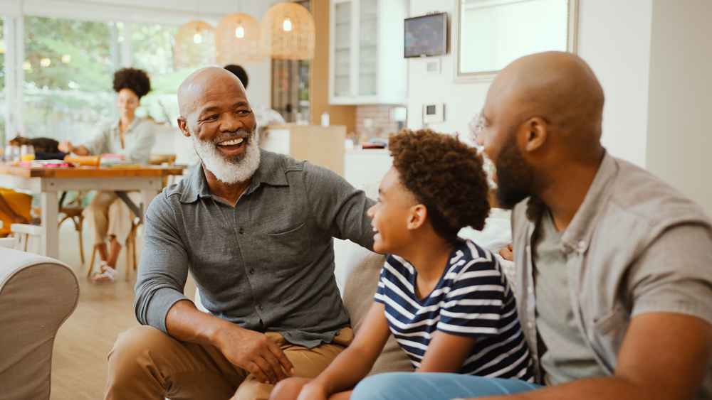 Laughing Multi-Generation Male Family Hanging Out On Sofa At Home Talking Together
